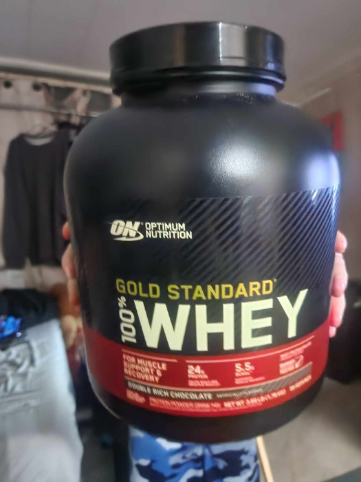 A kid holding a tub of gold standard whey protein powder.